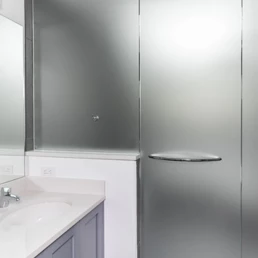 Eine Nahaufnahme eines Duschfensters, das mit einer matten Folie beschichtet ist und dem Badezimmer sowohl Privatsphäre als auch Stil verleiht.