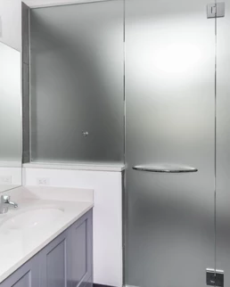 Une vue rapprochée d'une vitre de douche revêtue d'un film dépoli, offrant à la fois intimité et style à la salle de bains.