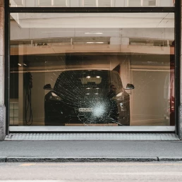 Une vitrine de concession automobile avec une vitre fracturée, évoquant des scènes de vandalisme ou d'accident.